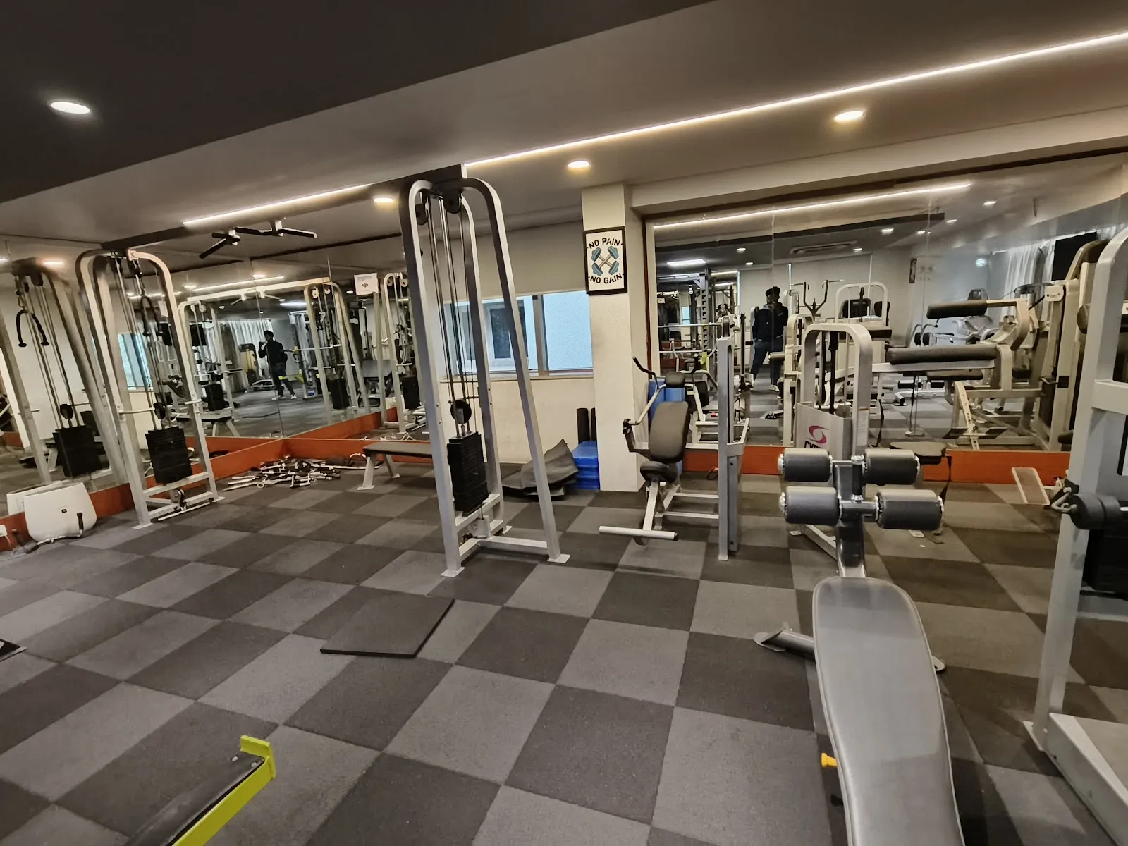 Floor of cable and selectorised machines and benches on chequered carpet tiles, mirror along the far wall