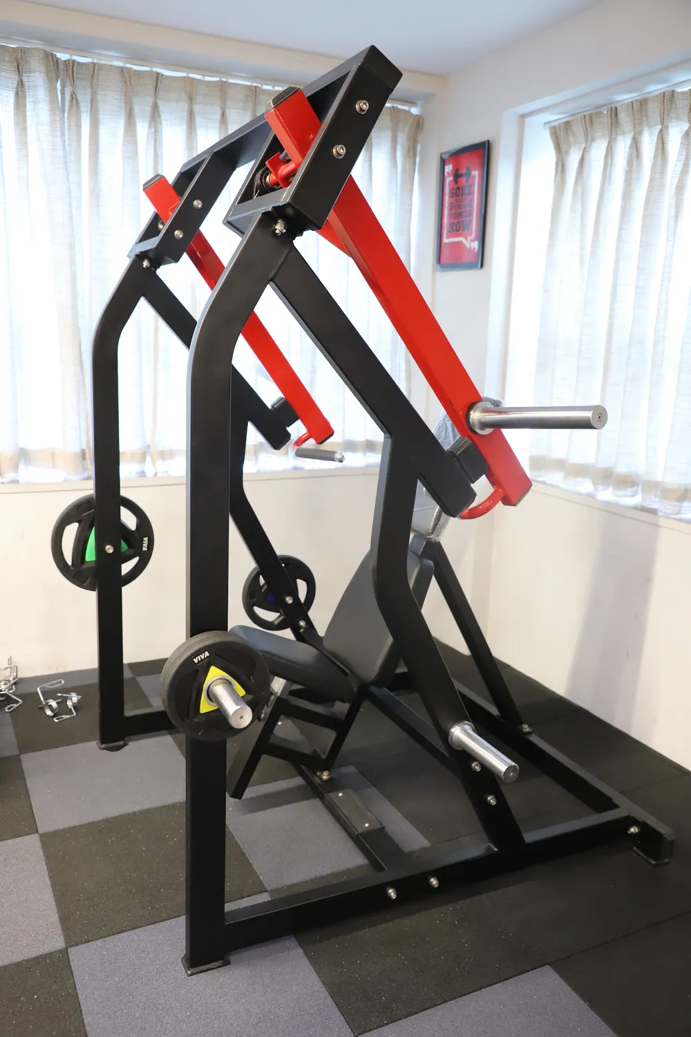 Black and red plate-loaded machine with weight plates on a grey carpet-tile floor